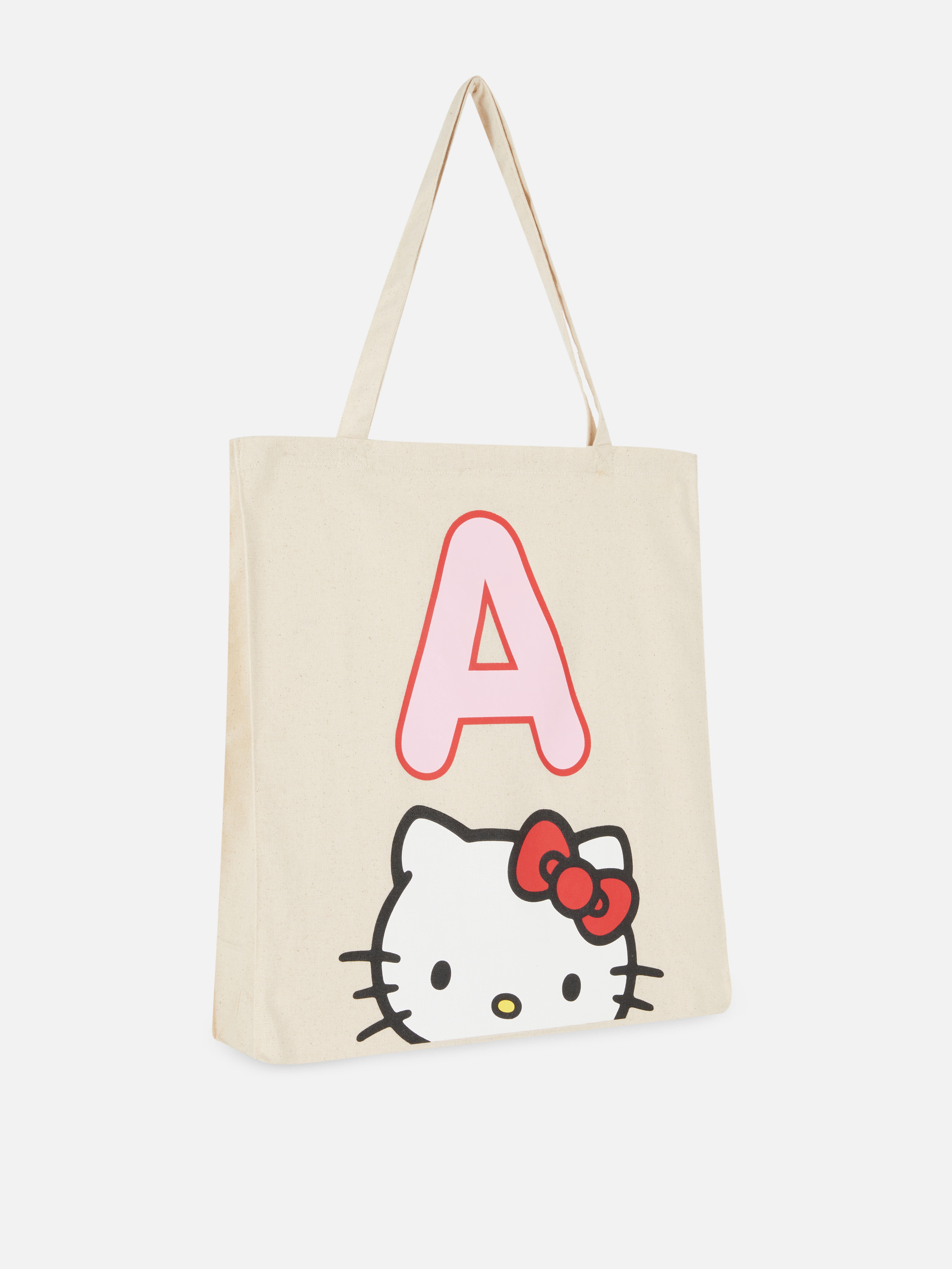 Geantă tote din pânză cu inițialele Hello Kitty. O geantă tote deschisă din pânză, cu două bretele de umăr și un design jucăuș cu Hello Kitty.