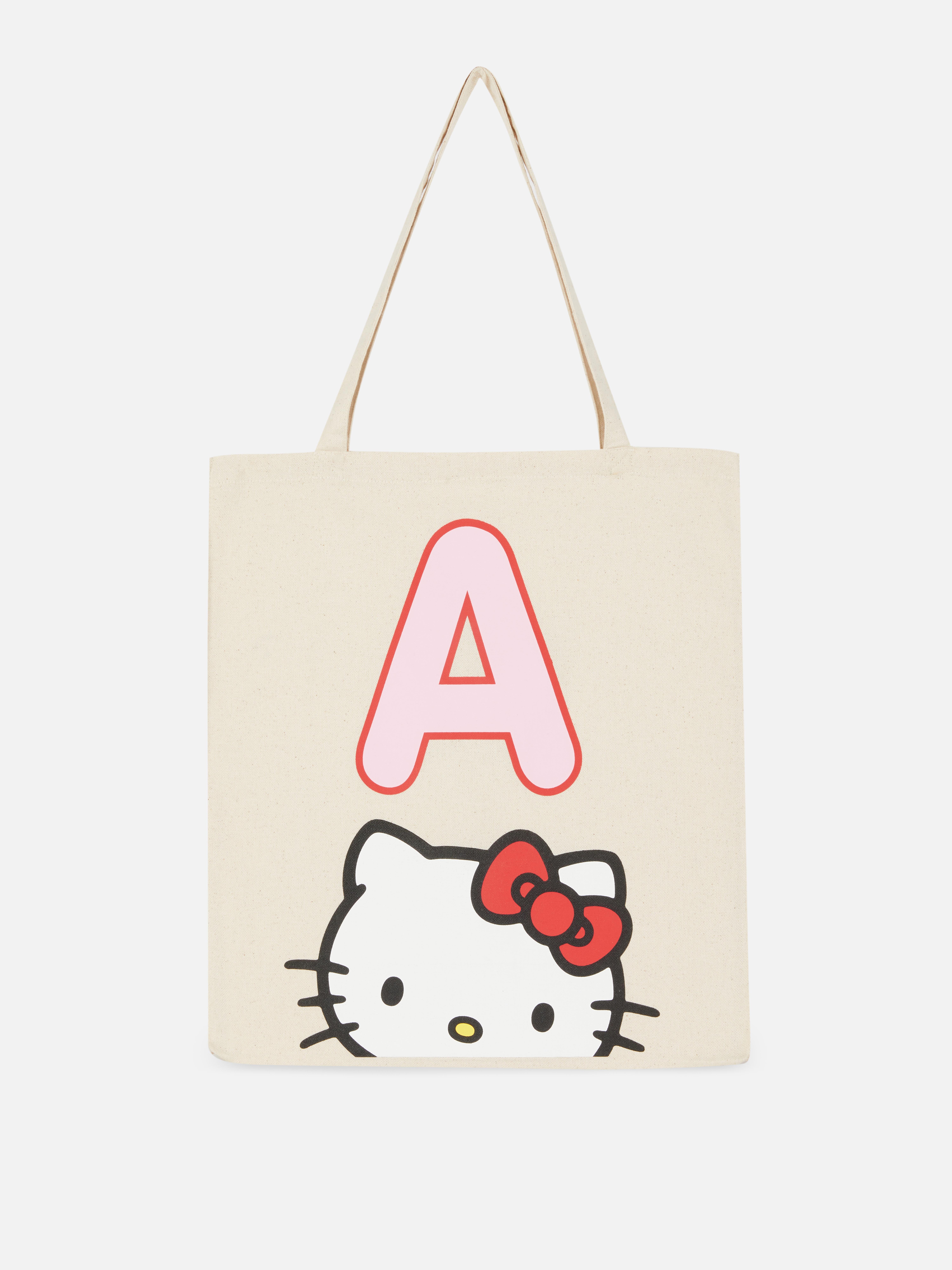 Τσάντα tote από καμβά με τα αρχικά της Hello Kitty. Μια ανοιχτή τσάντα tote από καμβά με δύο ιμάντες ώμου και ένα παιχνιδιάρικο σχέδιο Hello Kitty.