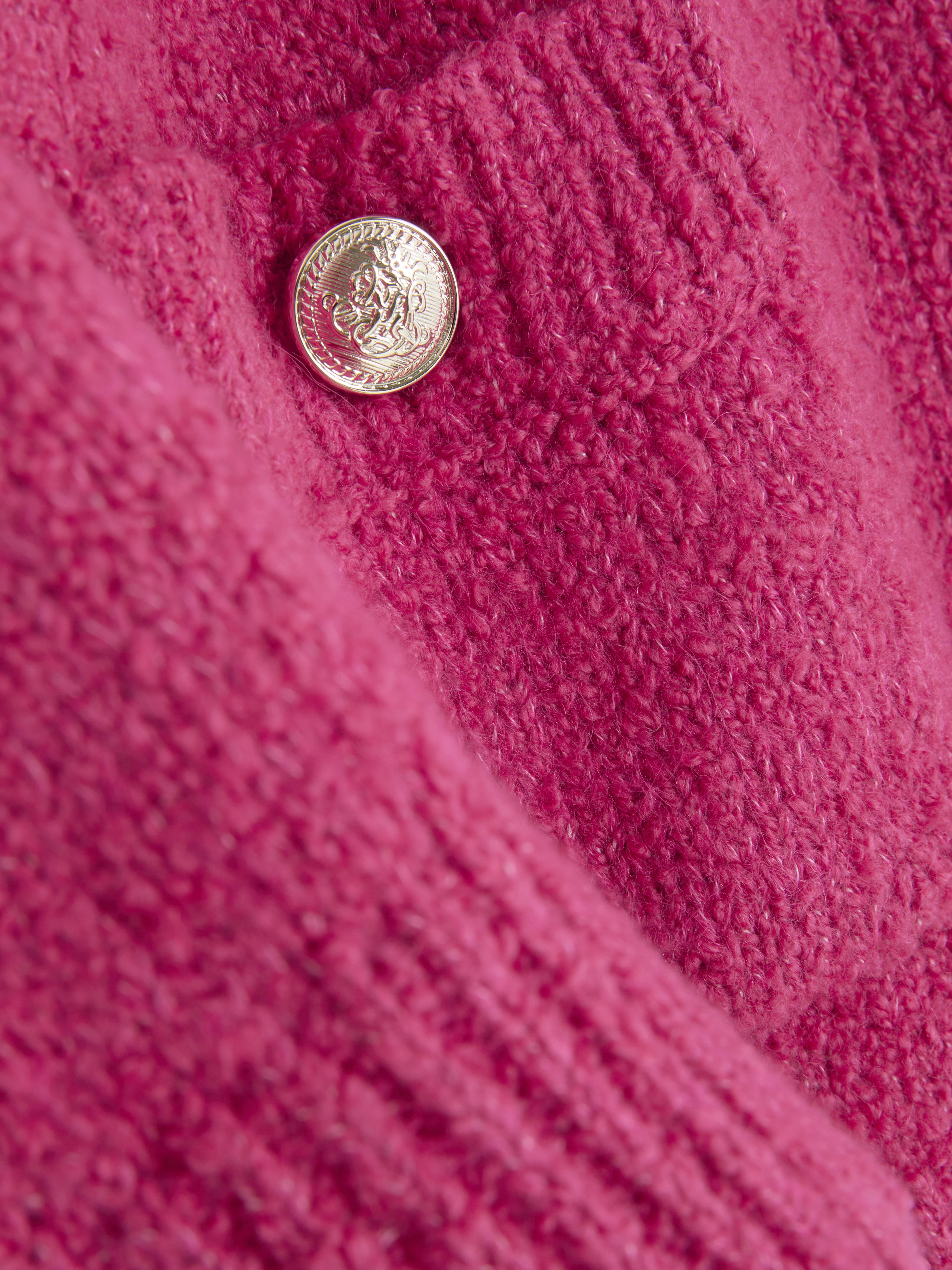 Bouclé-Strickjacke mit Knopfverschluss. Eine Strickjacke aus Bouclé-Stoff mit gerippten Bündchen, Knöpfen und aufgesetzten Taschen.