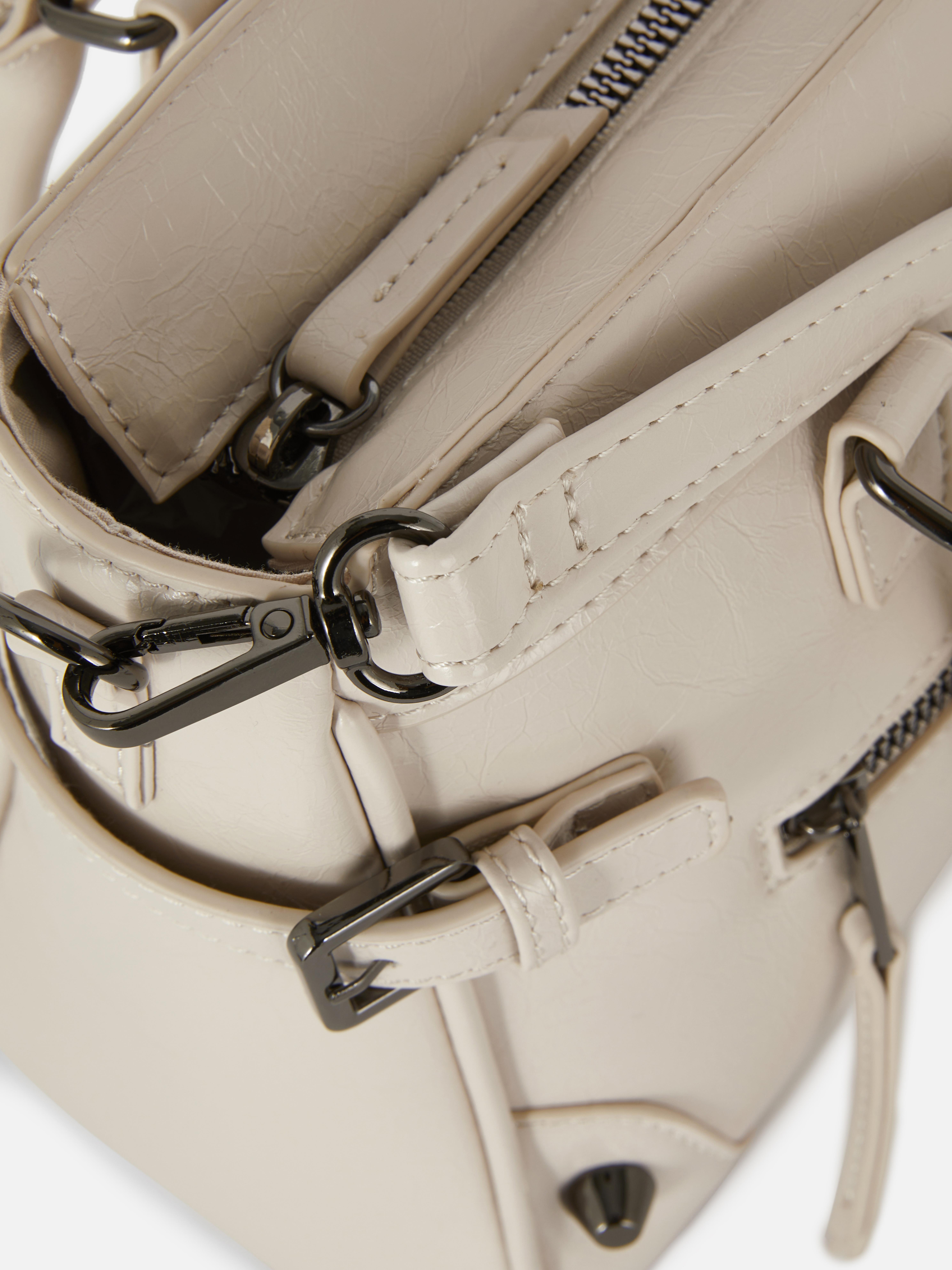 Abgenutzte Schultertasche aus Kunstleder. Eine mittellange Tragetasche aus Kunstleder mit Used-Look, mit Reißverschlusstaschen und Schnallendetails.