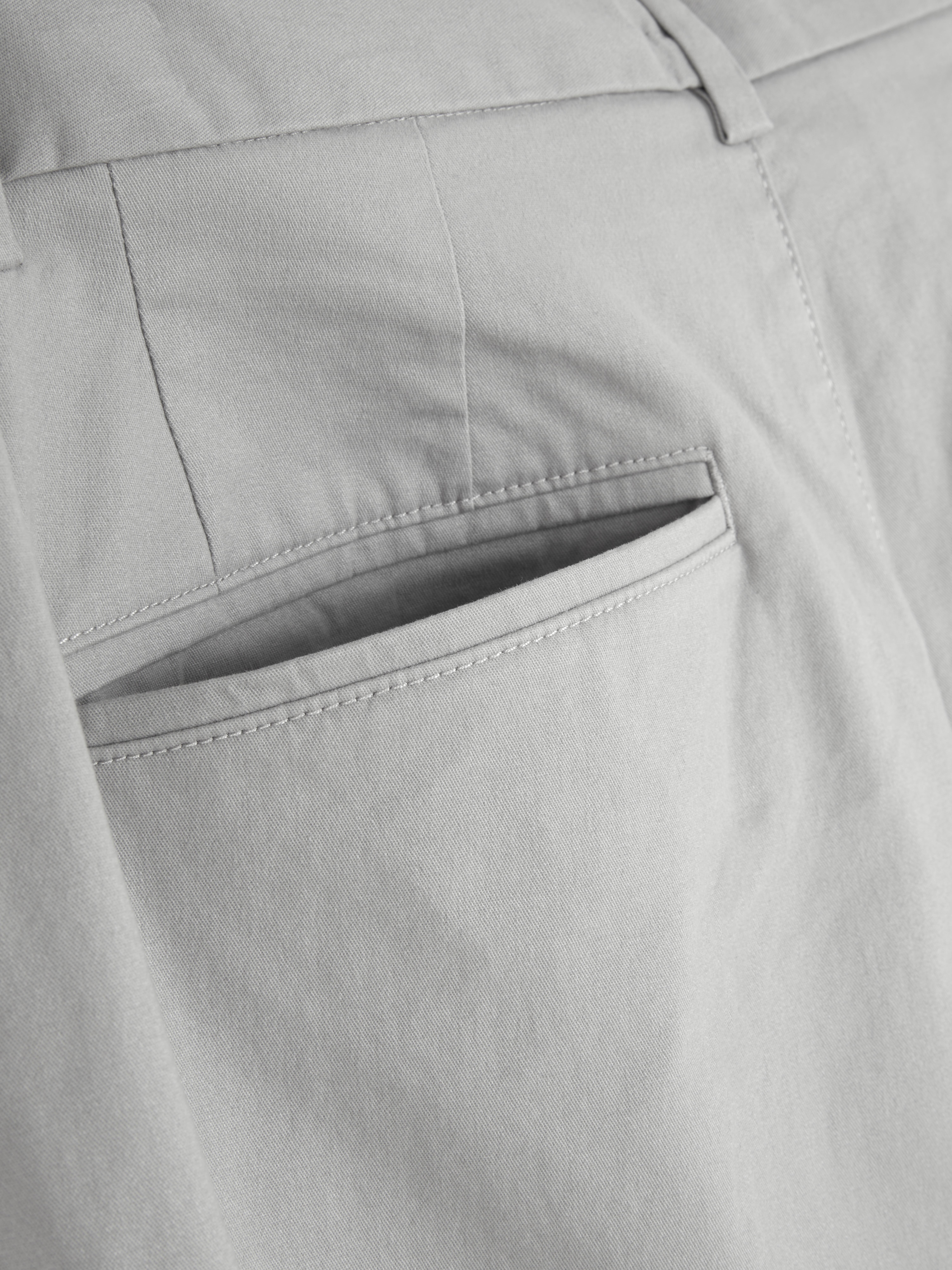Pantaloni chino elastici, mulați. Pantaloni chino mulați, confecționați în principal din bumbac și cu buzunare laterale.
