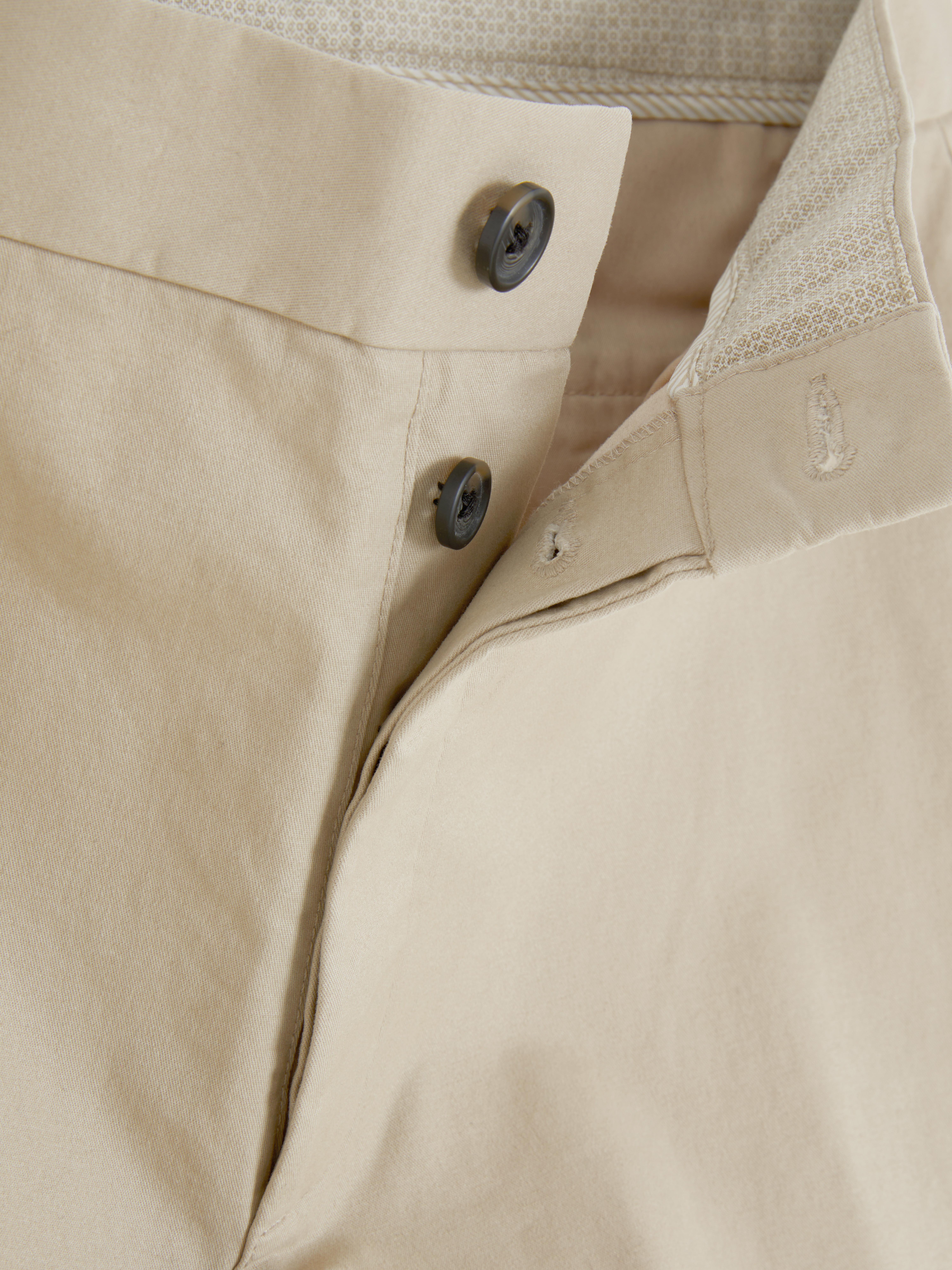 Pantaloni chino elastici, mulați. Pantaloni chino mulați, confecționați în principal din bumbac și cu buzunare laterale.