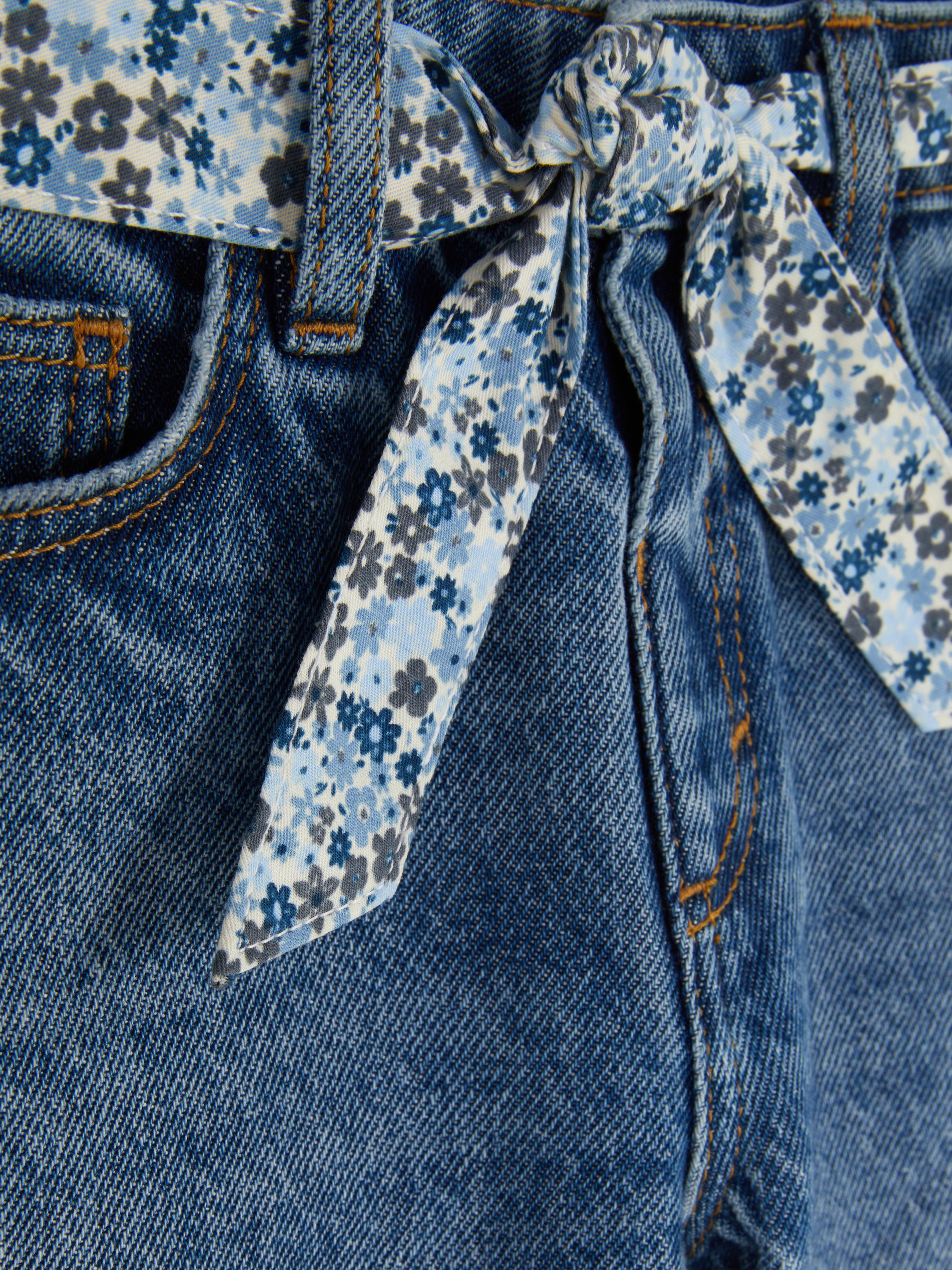 Jeans met gebloemde strikceintuur Een relaxte jeans met riemlussen, zakken en een gebloemde strikceintuur