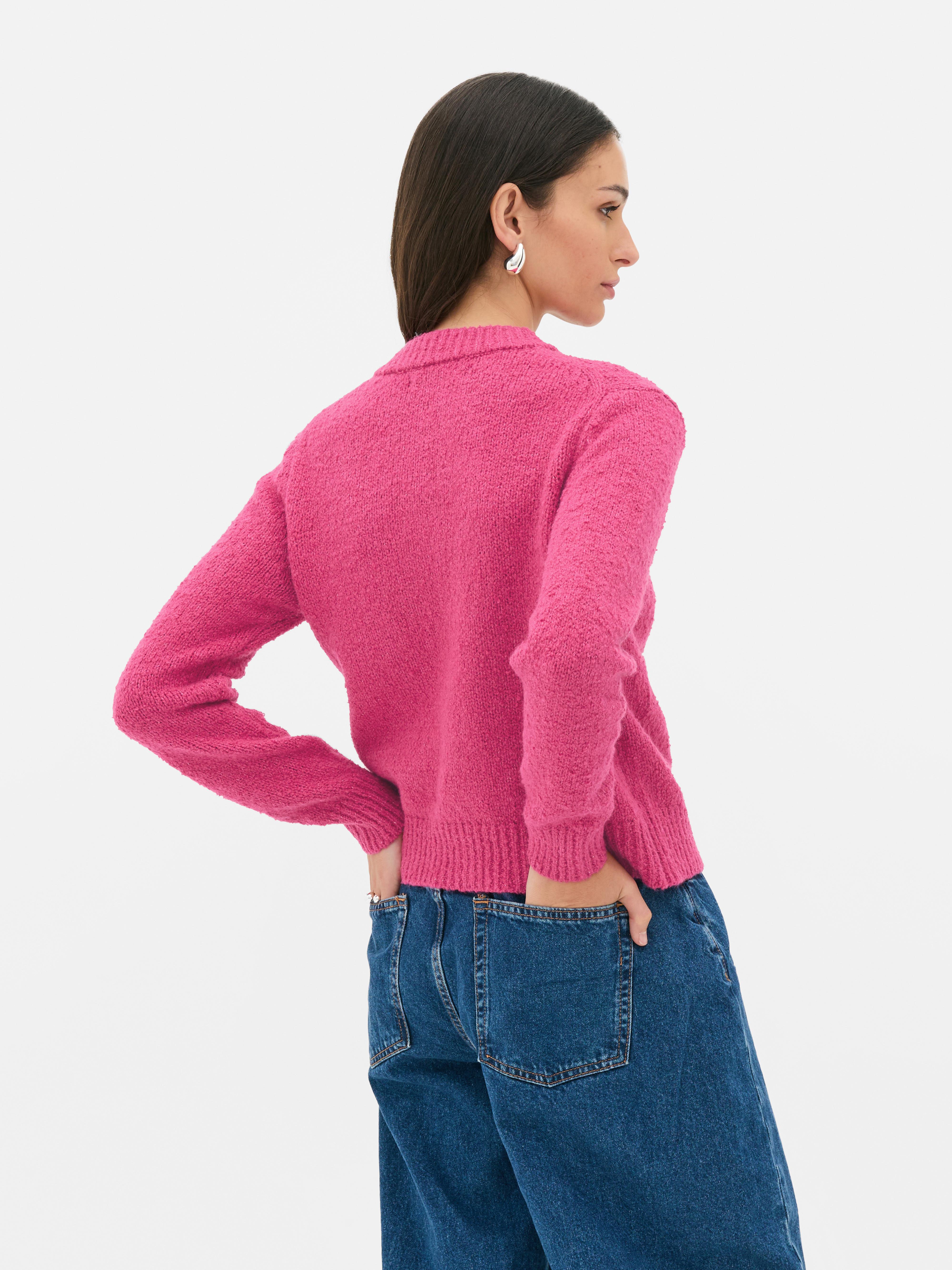 Bouclé-Strickjacke mit Knopfverschluss. Eine Strickjacke aus Bouclé-Stoff mit gerippten Bündchen, Knöpfen und aufgesetzten Taschen.