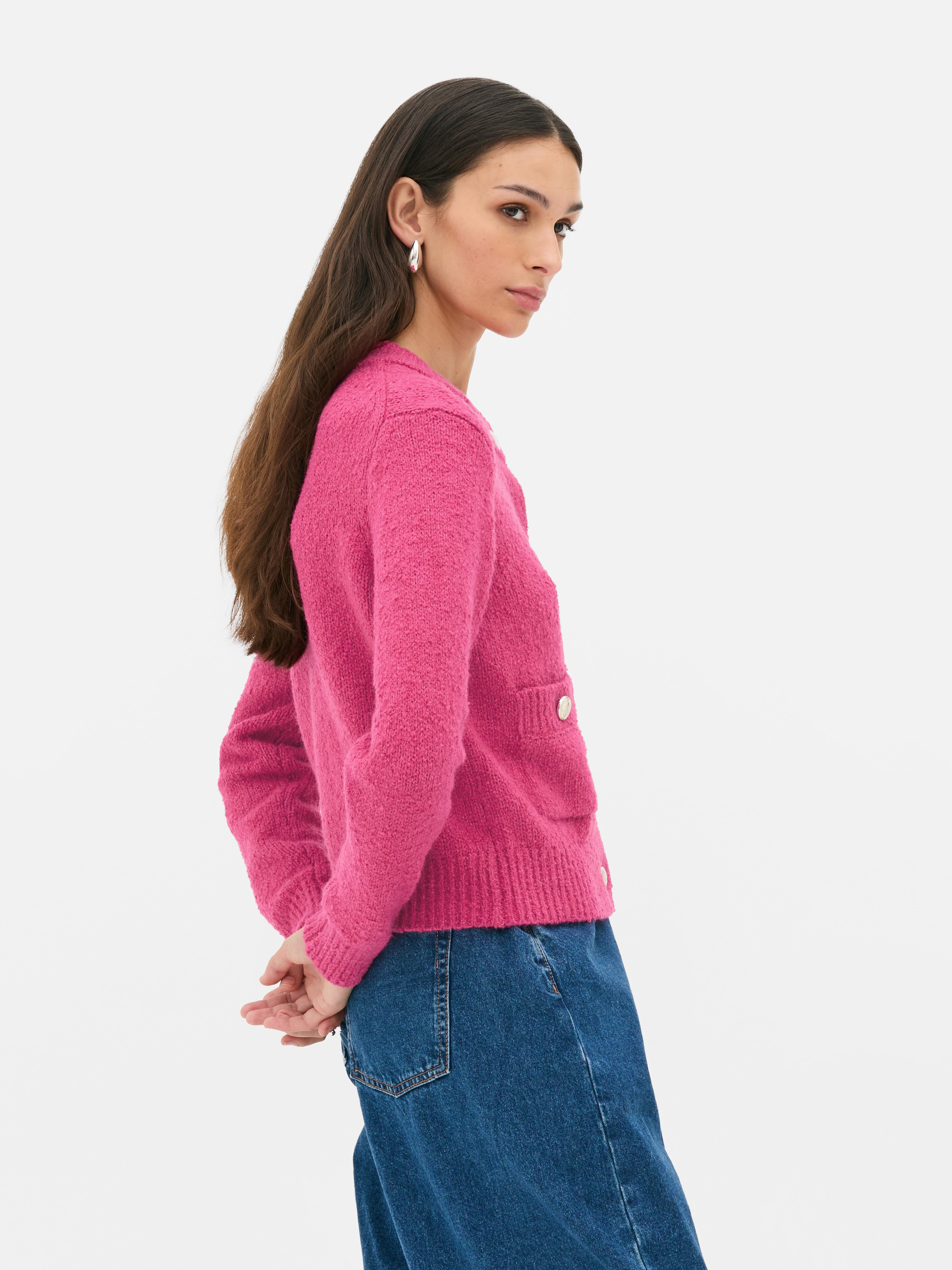 Bouclé-Strickjacke mit Knopfverschluss. Eine Strickjacke aus Bouclé-Stoff mit gerippten Bündchen, Knöpfen und aufgesetzten Taschen.