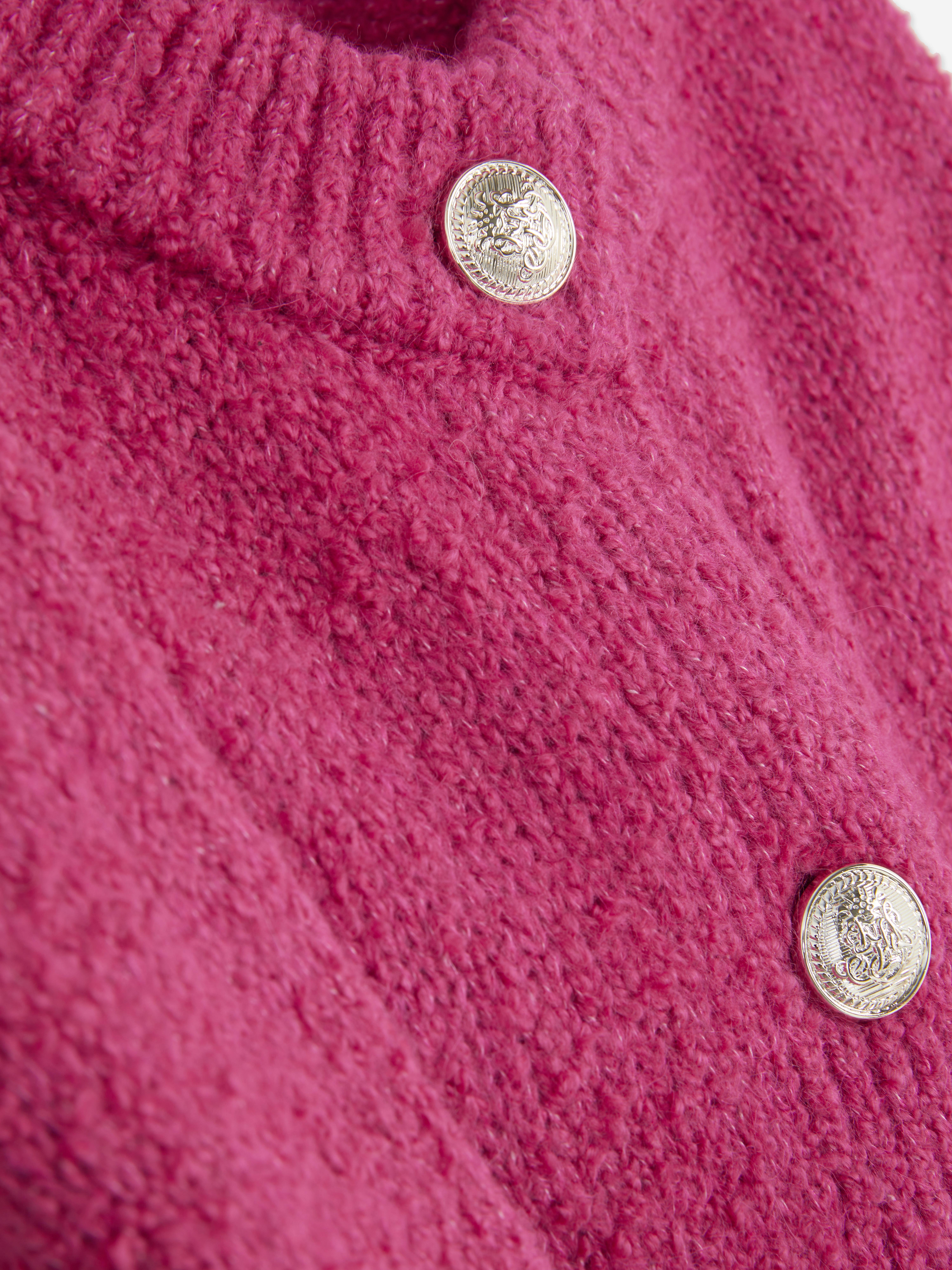 Bouclé-Strickjacke mit Knopfverschluss. Eine Strickjacke aus Bouclé-Stoff mit gerippten Bündchen, Knöpfen und aufgesetzten Taschen.