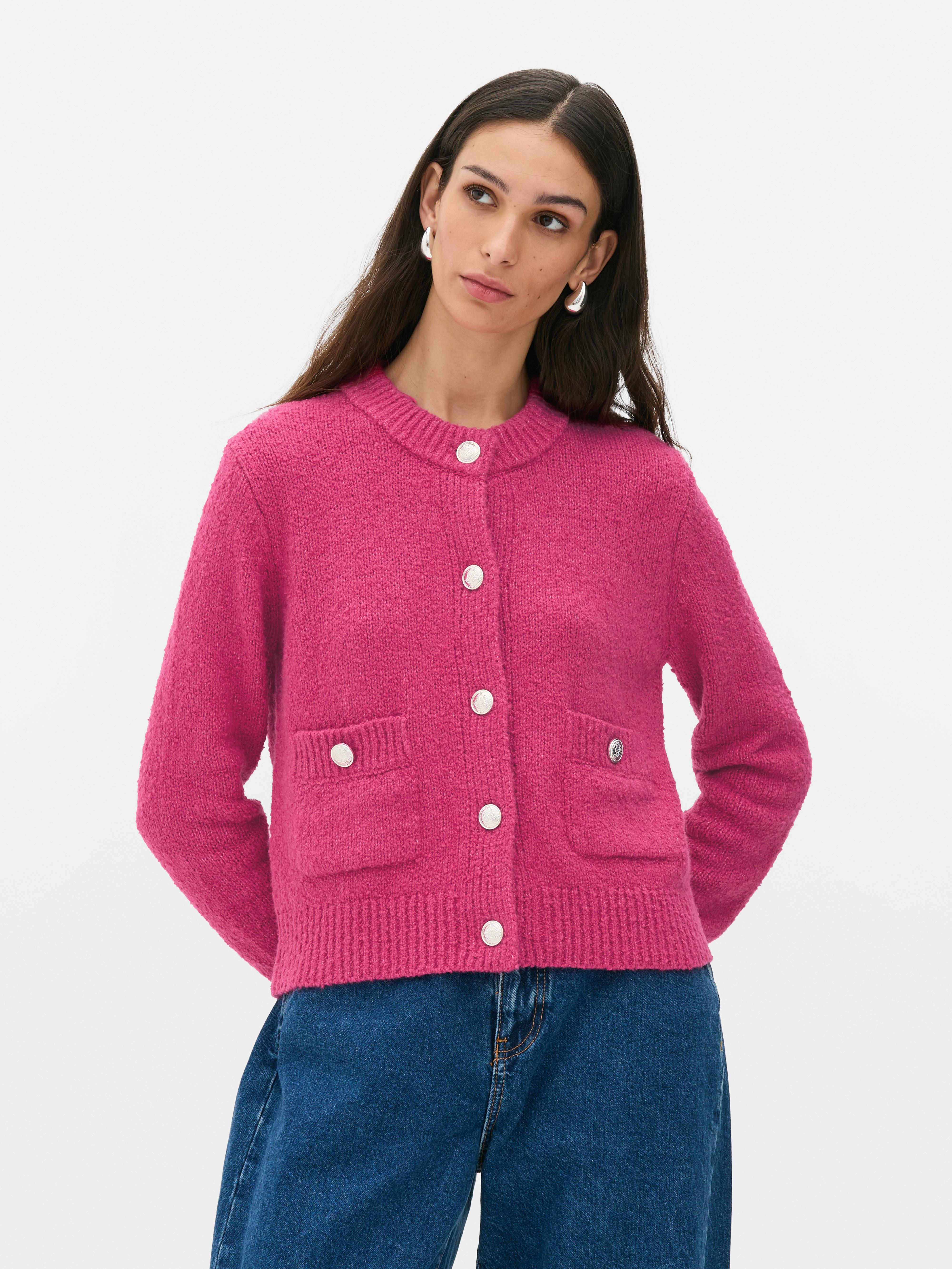 Bouclé-Strickjacke mit Knopfverschluss. Eine Strickjacke aus Bouclé-Stoff mit gerippten Bündchen, Knöpfen und aufgesetzten Taschen.