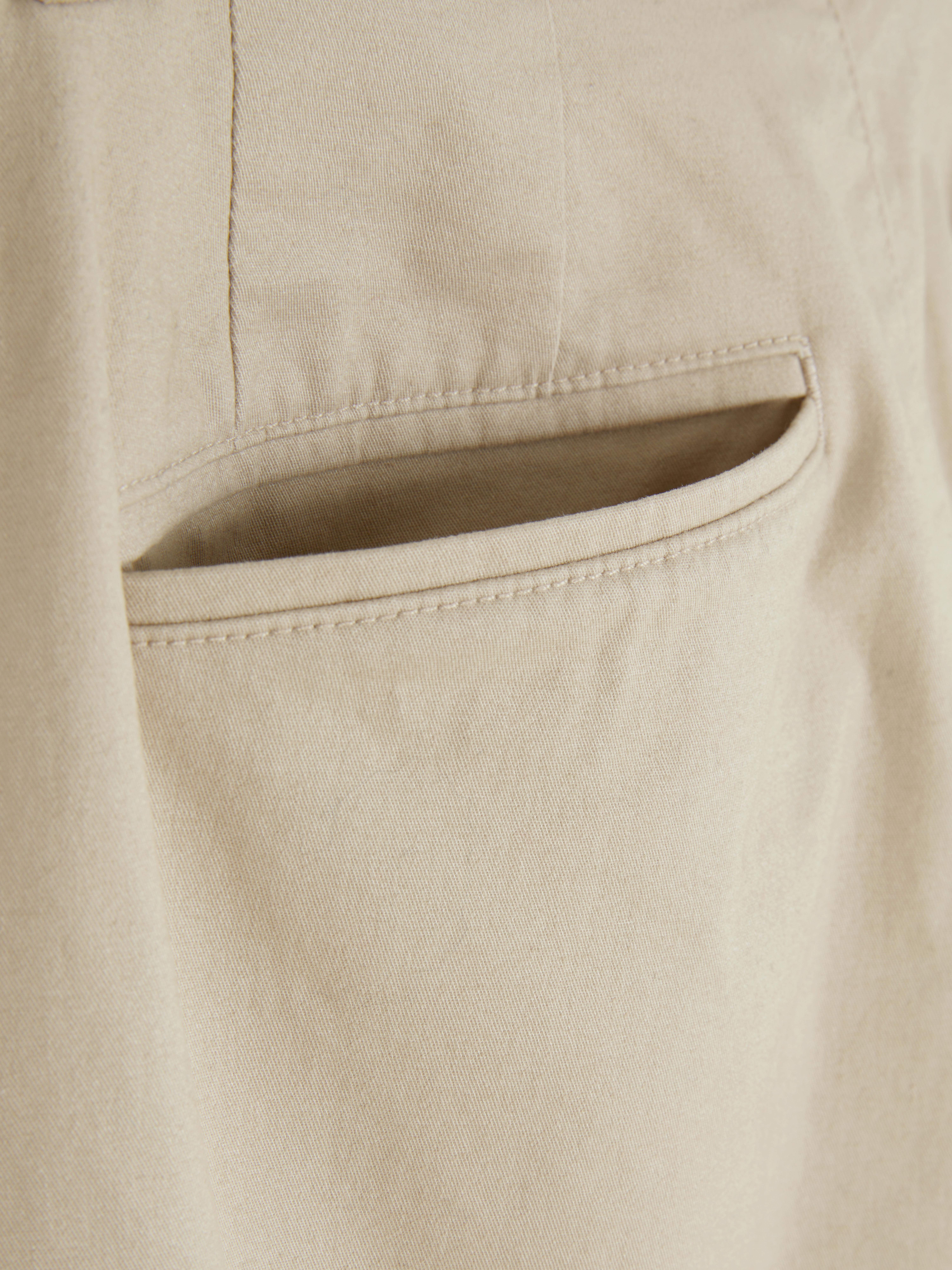 Pantaloni chino elastici, mulați. Pantaloni chino mulați, confecționați în principal din bumbac și cu buzunare laterale.